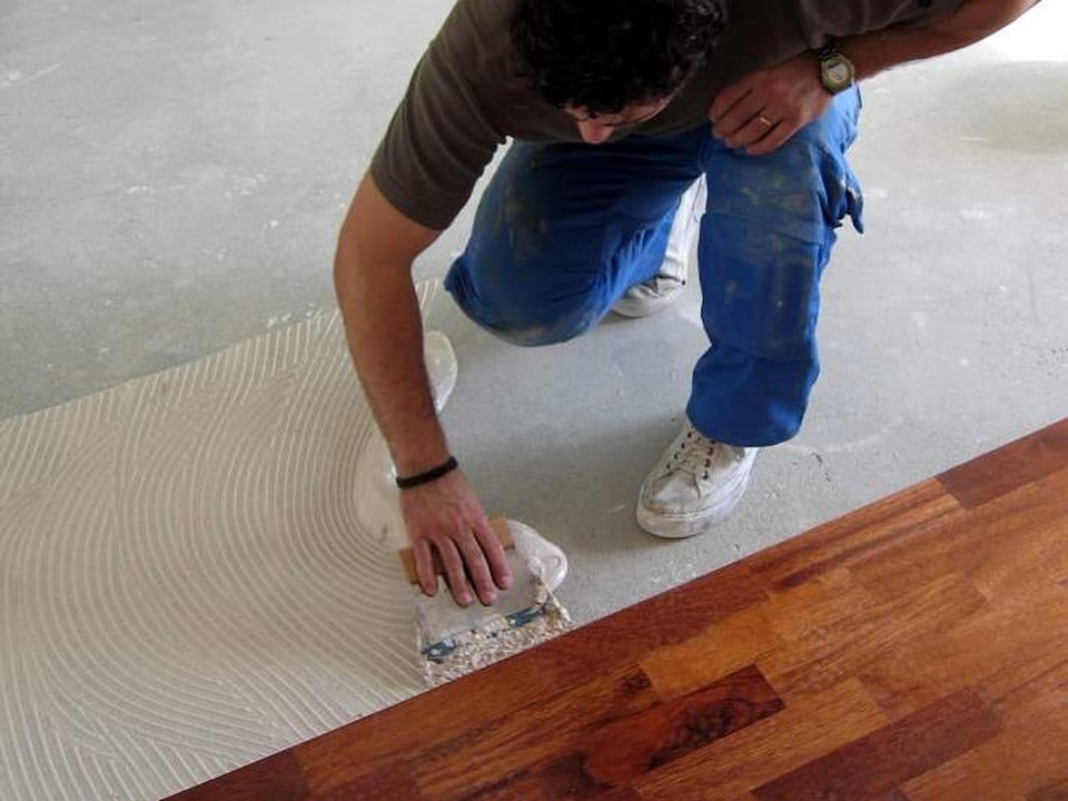 Installer spreading adhesive before laying timber floorboards