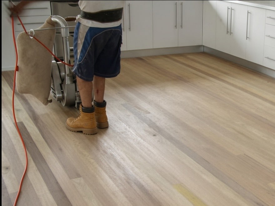 Person operating a floor sander on timber boards in a kitchen